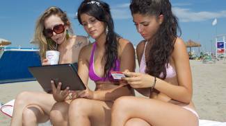 Tre ragazze in spiaggia alle prese con la tecnologia
